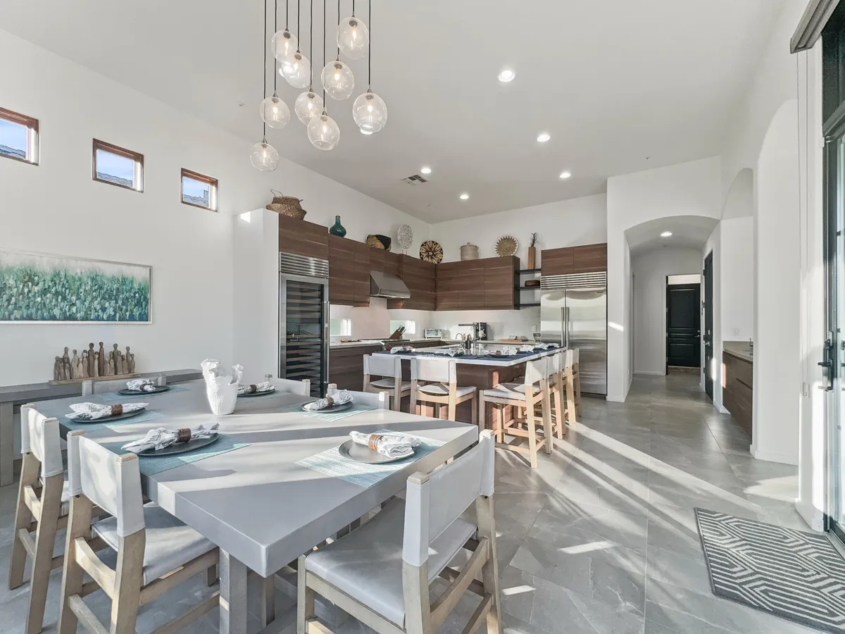 A welcoming kitchen and dining area featuring a large dining table set for a family meal, a kitchen island for cooking together, and elegant hanging light fixtures. The space is bathed in warm light, creating an inviting atmosphere for gatherings and everyday living.