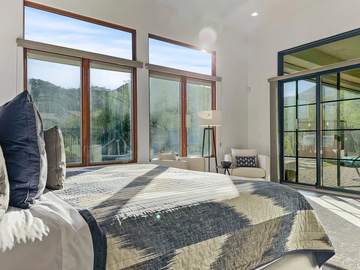 A serene king bedroom with patterned bedding, large windows letting in abundant natural light, and a cozy seating area. The room exudes comfort and calm, perfect for rest or quiet reading. The spacious layout and modern decor hints at the room's flexibility and luxury.