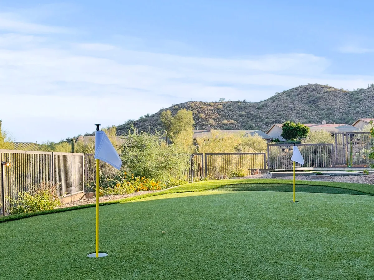 A view of a putting green bordered by flag poles and a fence, with expansive mountain views in the background. The area is open and inviting, suggesting opportunities for family activities and friendly golf competitions.