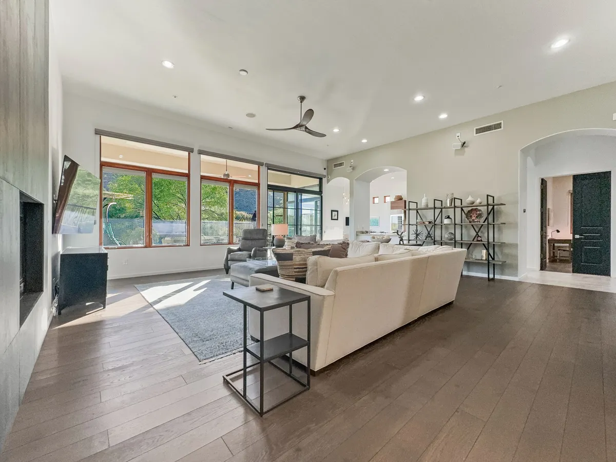 A bright, open living room with large windows that flood the space with natural light. Comfortable seating is arranged to invite conversation and relaxation, with sleek modern furnishings and a decorative shelving unit adding style. The expansive windows offer glimpses of mountain vistas, visually connecting the indoors with the scenic outdoors.