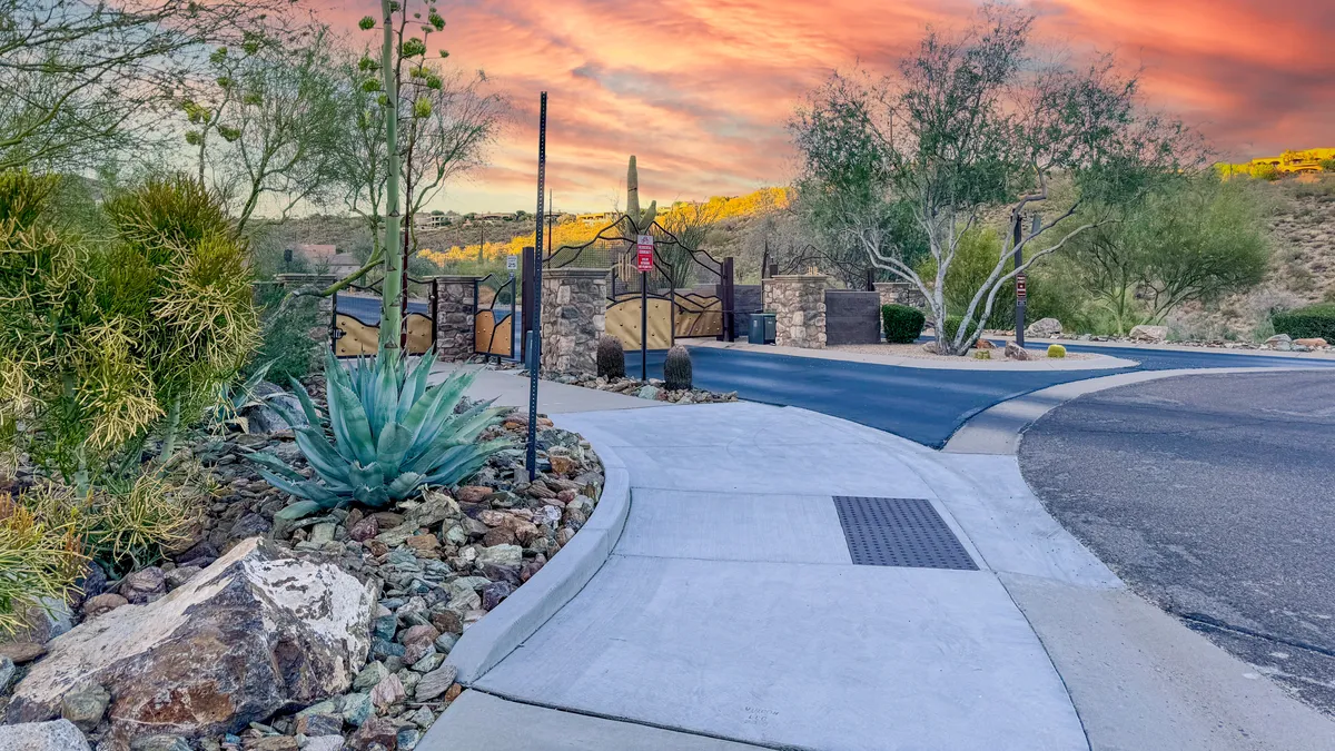 A serene exterior view featuring a gated entrance framed by cacti and a winding pathway leading into the property. The natural landscape and tranquil dusk lighting evoke a sense of privacy and security.