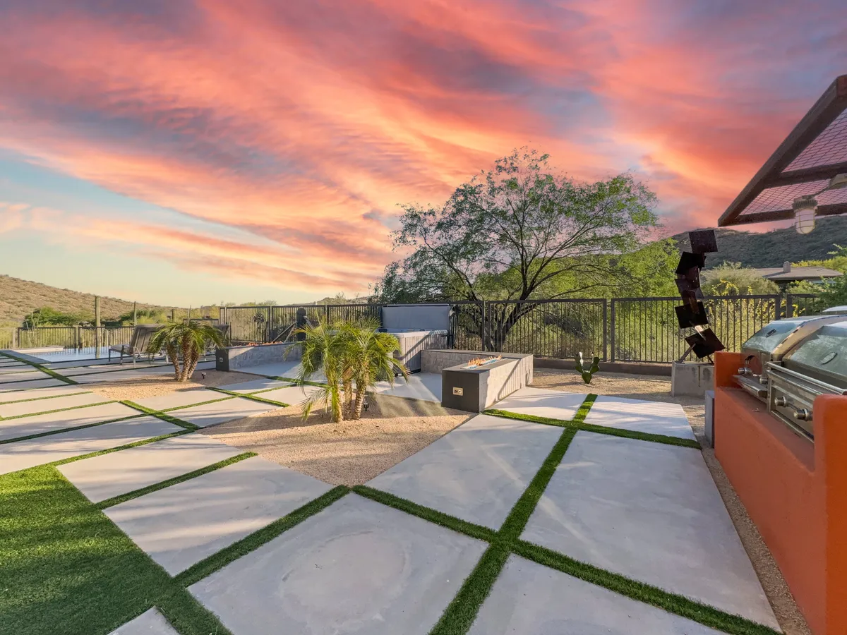 A modern outdoor kitchen and landscaped patio set beneath a vibrant sunset sky, flanked by palm trees. The space is perfectly designed for outdoor cooking, evening gatherings, and stargazing, offering a seamless extension of indoor comfort to the outdoors.