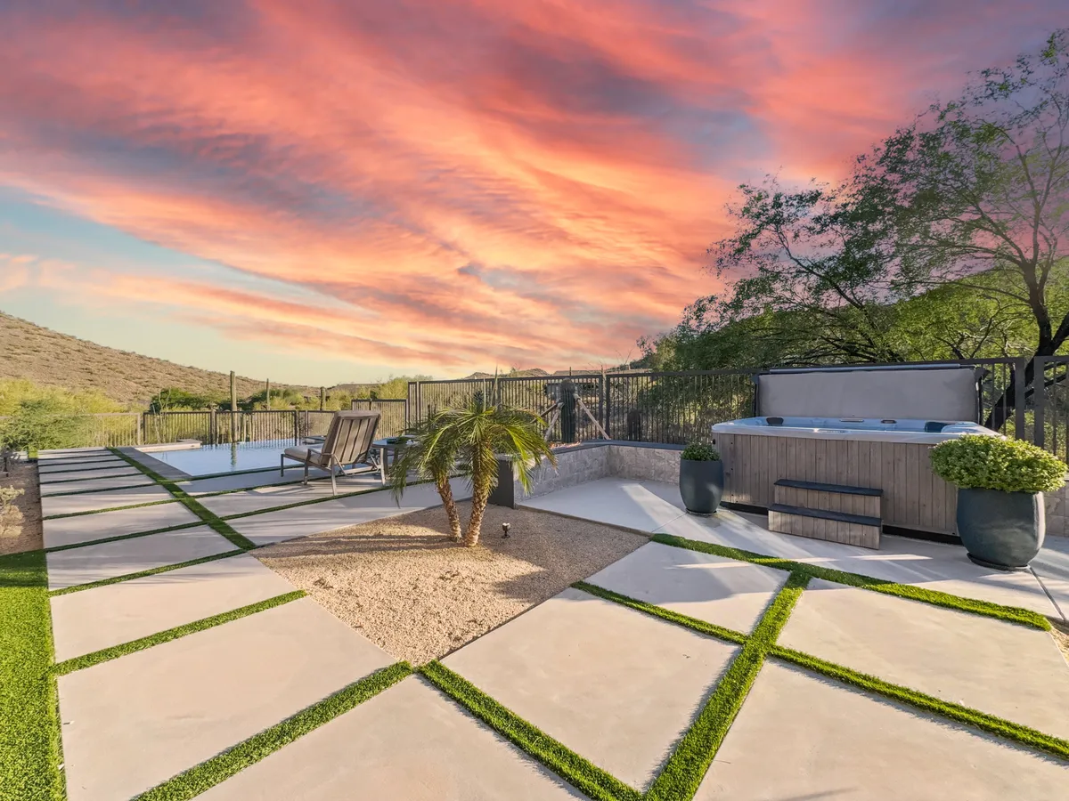 An inviting outdoor area with a luxurious hot tub, several lounge chairs for sunbathing, and decorative plants enhancing the landscaped paths. The scene is serene and ideal for both relaxation and social gatherings, especially in the evening light.