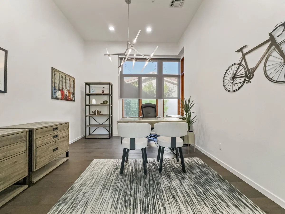 A private office setup with a modern desk and chair, a striking chandelier, bicycle wall art, and views of greenery through an open window. The ambiance is both productive and relaxed, supporting focused work or creative sessions.