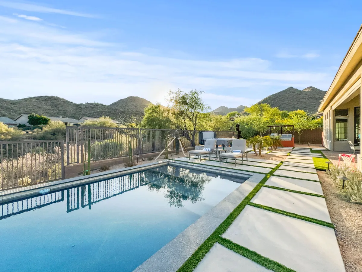 A sparkling swimming pool set against a stunning mountain backdrop, with a landscaped pathway and inviting patio seating. The tranquil outdoor scene is perfect for both daytime relaxation and sunset gatherings, reflecting the Arizona lifestyle.