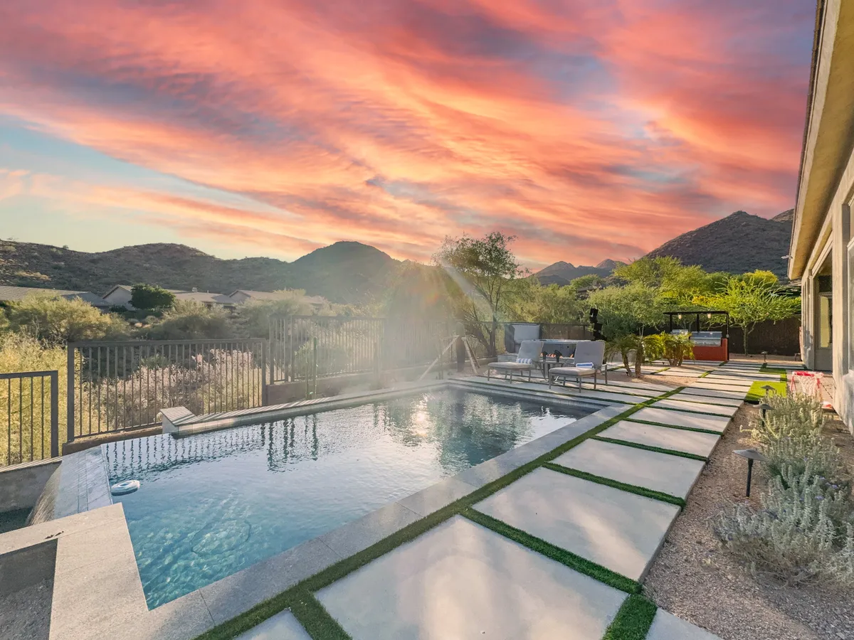 This exterior shows a stunning swimming pool with a mountain backdrop, sunset sky, and a relaxing patio area. The scene highlights both natural beauty and built-in amenities, inviting guests to enjoy memorable moments poolside—whether swimming, sunbathing, or stargazing from the patio.
