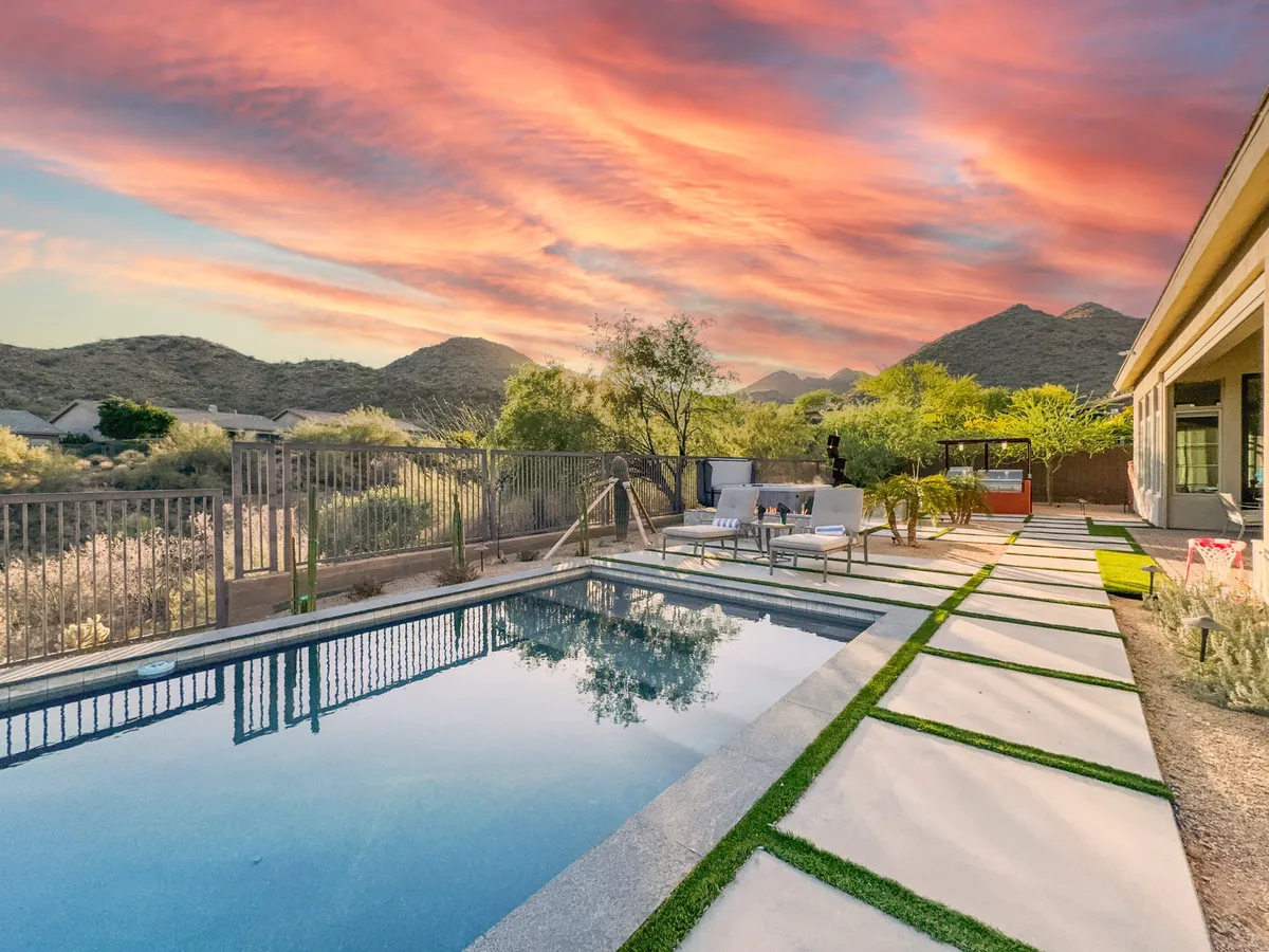 A beautiful exterior view showcasing a sparkling swimming pool surrounded by a tasteful outdoor seating area, set against an impressive mountain backdrop with a sunset sky. The setting is serene and inviting, perfect for relaxation, socializing, or enjoying the natural landscape while taking a break from work.